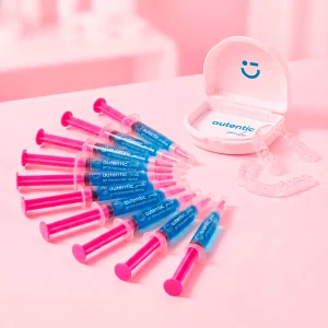 Kit de 10 jeringas de gel blanqueador dental Autentic Smile, con el estuche abierto y la férula transparente sobre fondo rosa