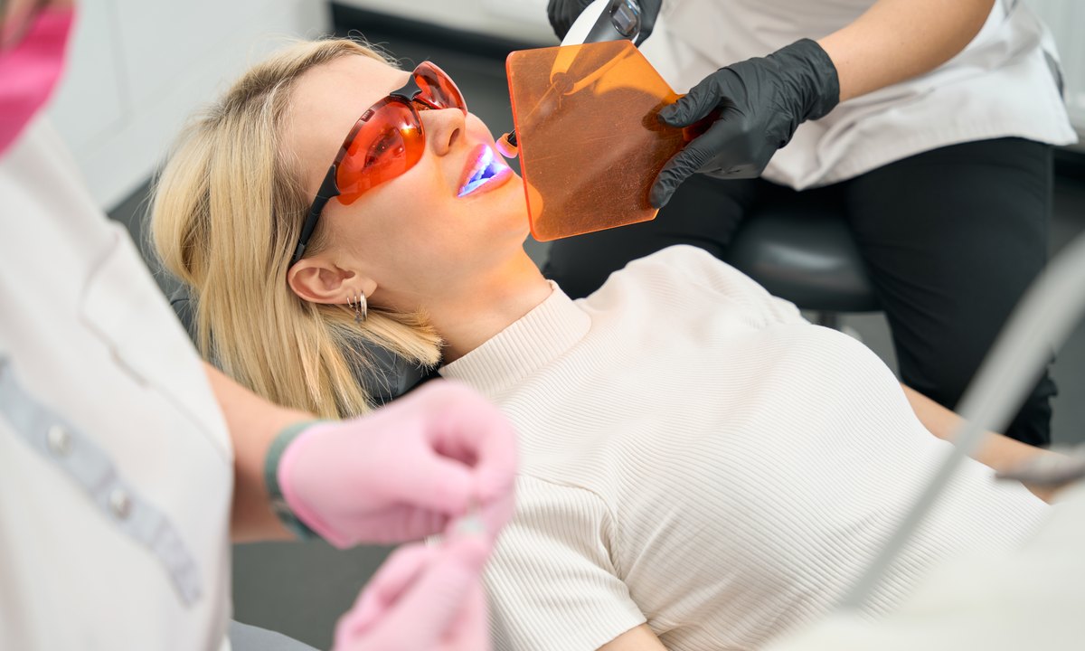 Precio del blanqueamiento dental con luz LED: sesión en clínica con gafas protectoras y pantalla naranja delante de la boca