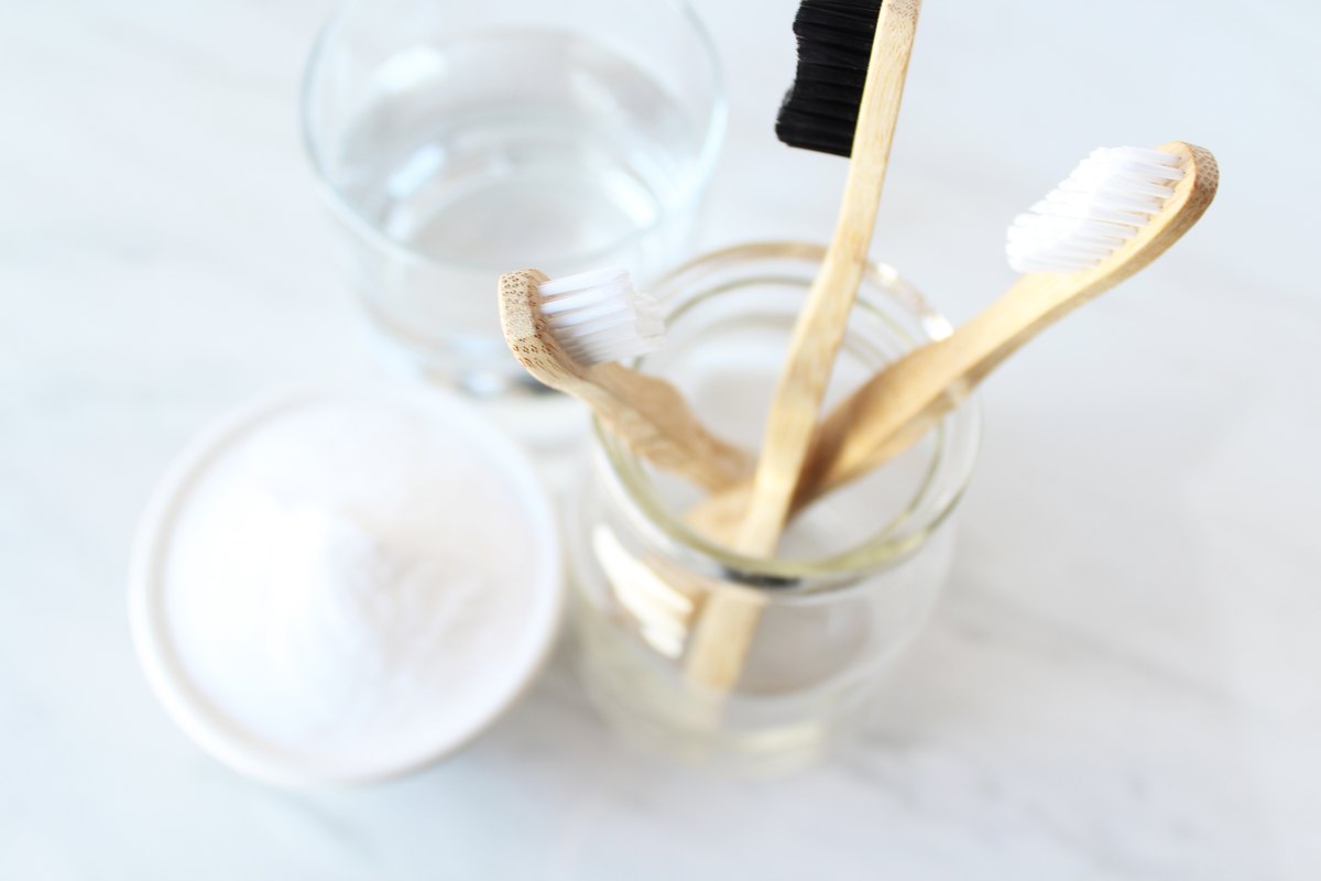 Bicarbonato en un cuenco, cepillos de dientes de bambú y un vaso de agua