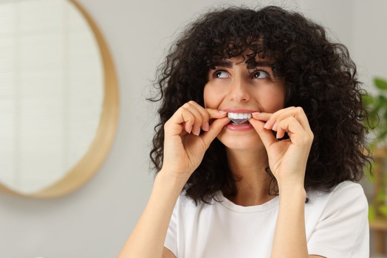 Blanqueamiento dental en casa: una mujer se coloca una tira blanqueadora sobre los dientes frente al espejo