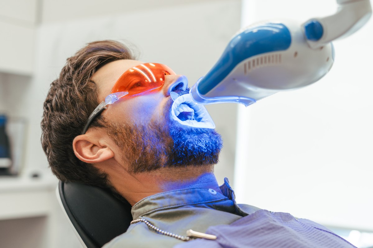 Blanqueamiento dental LED: paciente en el sillón con gafas protectoras bajo la lámpara de luz azul